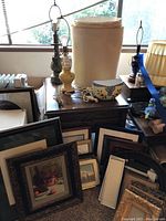 Photo showing assortment of vintage lamps, lamp shades, and various picture frames and framed artwork arranged on and around end tables.