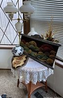 Overall view of floor lamp, end table with lace cloth and decorative pieces, framed textile artwork, and floral arrangement.