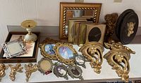 Overall view of gilt-style frames, mirrors, cherubs, and decorative items grouped on table.