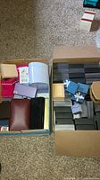 Two open boxes containing numerous empty jewelry boxes of various sizes and colors including black, brown, white, purple, beige, and pink.