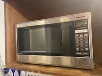Full view of Panasonic microwave oven showing stainless steel and black front, glass door, and shelves in the surrounding cabinetry.