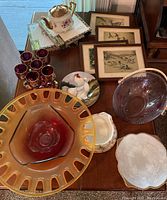 Top-down view of various glassware and decor including amber serving bowls, ruby glasses, teapot, rooster plate, white plates, and framed prints.