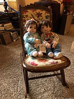 Two vintage Lola baby dolls sitting on a vintage small rocking chair.