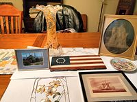 Lot overview showing the antique glass vase, framed pictures, American flag plaque, colorful plate, and Capiz shell floral decoration arranged on table