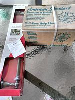 American Standard boxed bath spray and Delta boxed towel bar displayed on glass table.