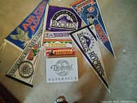 Triangular pennants and sports stickers featuring teams: Colorado Rockies, Denver Broncos, Denver Nuggets, Air Force Academy, Washington Redskins. The pennants have vibrant team logos and colors, arranged on a light carpet background.
