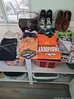 Photo showing folded women's clothing items including shirts, shorts, and skirt, two pairs of shoes, and a brown purse arranged on a table by a window.