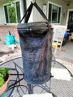 Front view of black nylon collapsible wildlife feeder bag with straps and zippered top, placed on outdoor table.