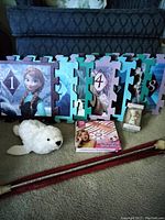 The full set of interlocking hopscotch puzzle pieces featuring Frozen characters, the plush seal, friendship bracelet kit box, and vintage baton with case all displayed on carpet