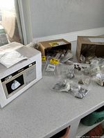 Box and multiple packages of various cabinet and drawer pulls and knobs on a countertop alongside a boxed light fixture