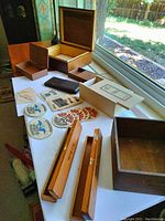 Photo of the wooden humidor box opened showing interior, various other wooden boxes, leather case, and several beer coasters laid out on a table near a window