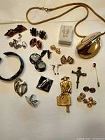 Photo shows a wide view of the assorted jewelry including earrings, pins, bracelet, and locket laid out on a white surface.