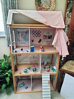 Front view of the large wooden dollhouse with fabric curtain pulled back showing three floors with dollhouse furniture and accessories arranged inside.