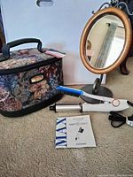 Photo showing standing oval wooden frame mirror, American Tourister tapestry toiletry case, and In Styler Max Wet to Dry hair styler with user manual on carpet.