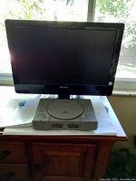 Philips TV and Sony PlayStation console together on a wood cabinet in front of window