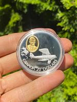 Coin in clear protective capsule, front view showing silver plane design and gold portrait insert