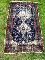 Full view of antique Boho style carpet laid out on grass showing central medallion pattern and overall wear
