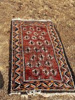 Full view of the antique boho style handwoven carpet laid on dry grass showing overall pattern and condition.