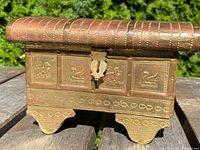 Front view of the antique Middle Eastern hand hammered copper bound table box showing the metal lock plate and animal motifs embossed on the panels.