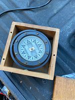 Compass inside original wooden box with lid removed. Shows compass face and surrounding black metal housing.