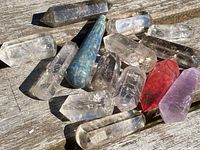 Collection of pointer crystal geodes on wooden surface showing variety of colors and sizes including clear, smoky, blue, red, and pink crystals