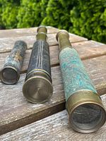 Three cylindrical items on wooden surface: small collapsed tube or sleeve roll, black leather–wrapped telescope, verdigris-covered telescope