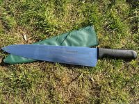 Full view of knife with blade resting on green sheath on grass.