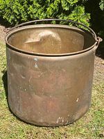 Front-side view of large antique copper cauldron with visible dents and patina, showing handles and curved top handle.