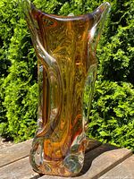 Front angle showing amber glass vase with clear overlays and sculptural chalet style design in daylight outdoors