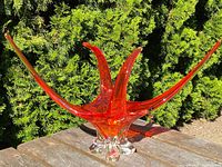 Angled front view of red glass chalet sculpture on outdoor wooden surface