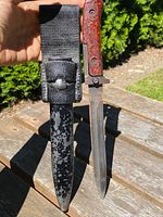 Full view of military knife with reddish-brown handle and original black sheath showing surface wear and matching numbers.