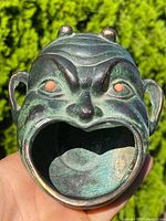 Frontal view of bronze head-shaped ashtray showing open mouth basin, coral eyes, surface patina