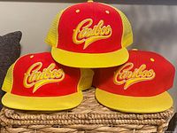 Three vintage Cariboo hats stacked on a woven basket, showing red front panels, yellow brims and yellow mesh backs.