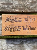 Close up photo of one side of the wooden box showing Coca Cola logos in various languages including U.S.S.R., Japan, Canada, and Thailand.