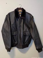 Full view of dark brown leather bomber jacket with fur collar hanging on wood hanger.