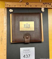 Brown leather case with brass plate on wooden base, showing overall size with rulers for scale.