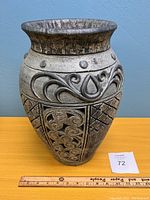 Front view of a decorative ceramic vase showing swirl and teardrop patterns with a ruler for scale approximately 12 inches tall.
