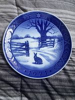 Blue and white collector plate dated 1971 with winter scene depicting a rabbit, fence, leaf pattern border on porcelain plate.