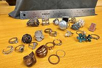 Photo showing 18 costume jewelry rings arranged in two rows with a ruler for scale.