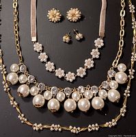 Mixed goldtone and faux pearl costume jewelry including three necklaces and two pairs of earrings displayed against a dark background.