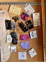 Overview of assorted earrings on display board and cards, displayed on wooden board, showing different sizes and styles including hoops, dangles, drops, and studs