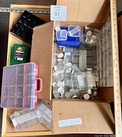 Top-down view of the box filled with various empty plastic craft storage containers, including multi-compartment organizer boxes, small jars with white lids, and a pink portable organizer.