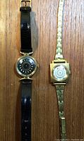 Two wristwatches, one with black leather strap and black dial featuring a geometric kaleidoscope pattern, one with gold-tone metal bracelet and white dial with kaleidoscope pattern. Watches laid flat on wood surface.