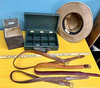 Photo of all items on yellow surface showing leather hat, belts, two wooden trinket boxes, wooden duck figurine, and collector coin