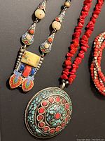 Close-up image of colorful silver-tone necklace with turquoise, red coral, lapis lazuli inlay and surrounding beads, and multi-strand red coral chip necklace.