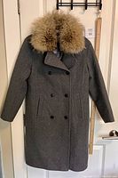 Full front view of the grey wool coat with removable raccoon fur collar on door with ruler for size reference.