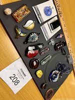 Top-down photo of 16 assorted art glass and costume jewelry pendants arranged on a black board with a ruler for scale