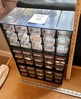 Front angle view of parts organizer showing clear plastic drawers, labels, and black/gray frame with a ruler for scale.