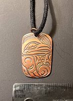 Rectangular metal pendant with indigenous eagle design shown with ruler for size reference.