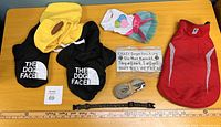 Top view of small to extra small dog clothes, leashes, and a decorative sign on a wooden table.
